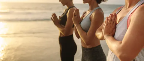 Women in a yoga pose with hands at heart center on a beach